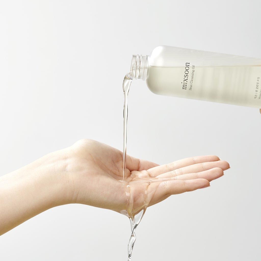 Flacone di Mixsoon Bean Cleansing Oil che versa l’olio detergente sul palmo della mano su sfondo neutro