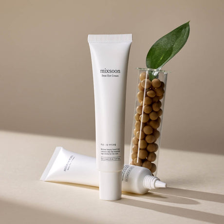Mixsoon Bean Eye Cream in tubetto su superficie chiara, con secondo tubetto aperto e fagioli in provetta con foglia decorativa sullo sfondo
