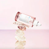 Flacone del siero SKIN1004 Madagascar Centella Pink Ampoule adagiato su una pila di cristalli naturali trasparenti, con sfondo rosa chiaro.