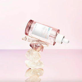 Flacone del siero SKIN1004 Madagascar Centella Pink Ampoule adagiato su una pila di cristalli naturali trasparenti, con sfondo rosa chiaro.