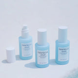 Tre flaconi azzurri della linea SKIN1004 Centella Hyalu-Cica su sfondo bianco, con uno dei flaconi aperto e il tappo appoggiato a lato.