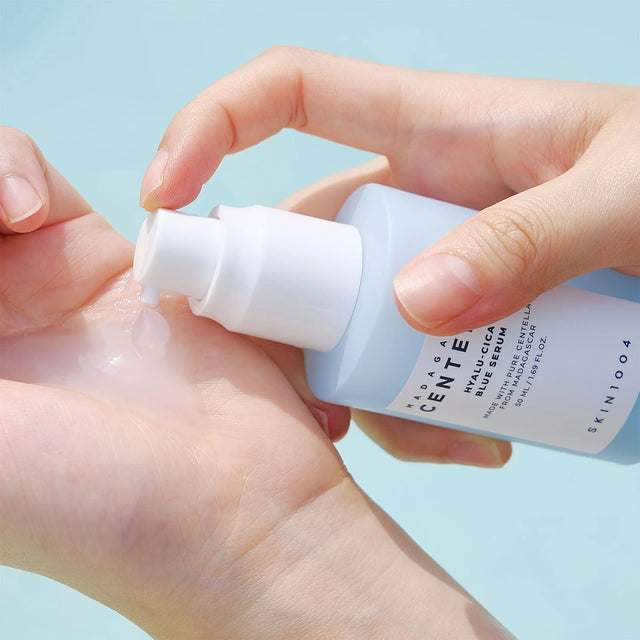 Mano che eroga il siero SKIN1004 Centella Hyalu-Cica Blue Serum sulla pelle del palmo, con sfondo azzurro chiaro.