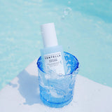 Flacone del siero SKIN1004 Centella Hyalu-Cica Blu Serum immerso in un bicchiere d’acqua trasparente con schizzi, su sfondo azzurro.