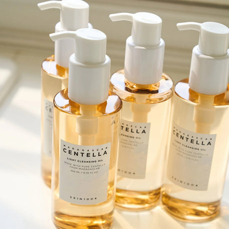  Quattro flaconi del detergente SKIN1004 Madagascar Centella Light Cleansing Oil da 200ml con pompa bianca, disposti su superficie chiara con luce naturale.