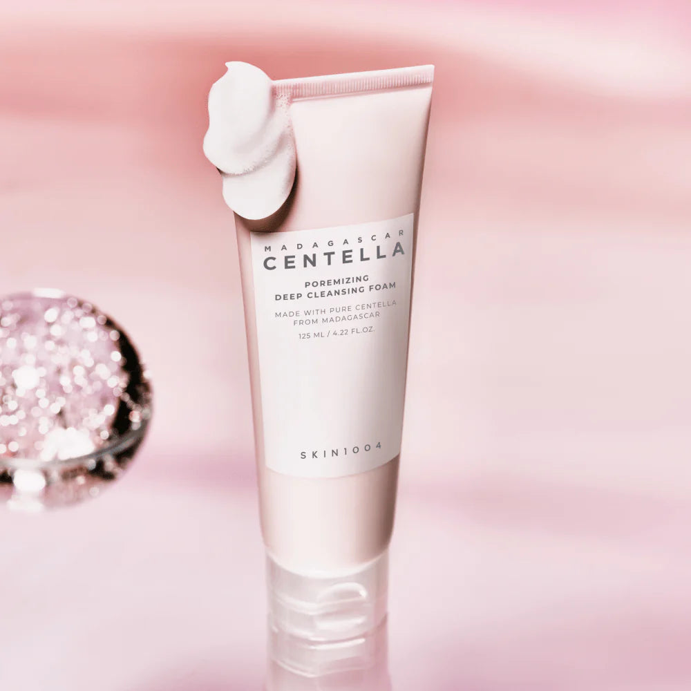 Tubo da 125ml del detergente SKIN1004 Madagascar Centella Poreminizing Deep Cleansing Foam con una dose di prodotto schiumoso sulla parte superiore, su sfondo rosa perlato.