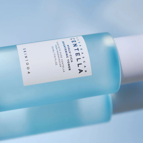Flacone azzurro trasparente del tonico SKIN1004 Centella Hyalu-Cica Brightening da 210ml sdraiato su sfondo azzurro con riflessi di luce