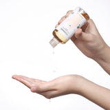 Mano che versa alcune gocce di Mixsoon Soondy Centella Asiatica Essence su un palmo aperto. La bottiglia è inclinata e decorata con un orso stilizzato. Sfondo bianco, atmosfera pulita e minimalista.

