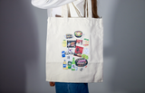Persona con camicia bianca fotografata di profilo mentre indossa una tote bag color panna con illustrazioni di cibo e prodotti coreani stampate frontalmente
