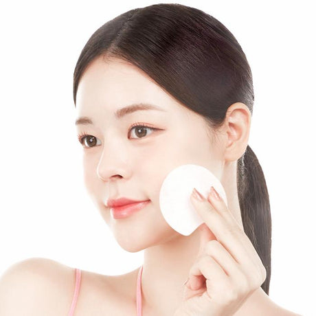 Modella che applica un dischetto toner pad sul viso su sfondo chiaro