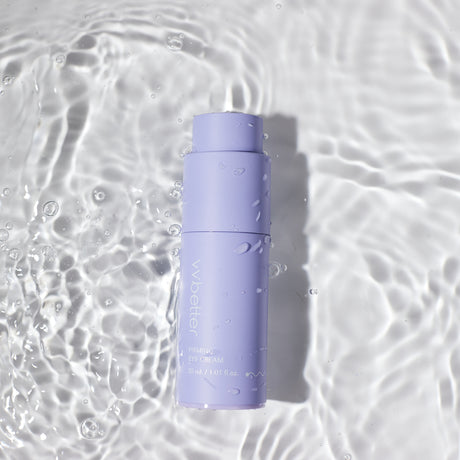 Flacone color lavanda del vvbetter Firming Eye Cream da 30 ml / 1.01 fl.oz., adagiato su una superficie d’acqua con riflessi e gocce visibili, evocando una sensazione di freschezza e idratazione.