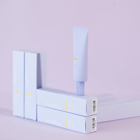 Un tubetto di vvbetter Daily Airfit Sunscreen SPF 50+ PA++++ è posizionato in verticale sopra la sua confezione, con altre scatole allineate in secondo piano. L’intera scena ha uno sfondo lavanda minimalista, creando un effetto visivo pulito ed elegante che richiama la delicatezza del prodotto.