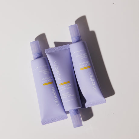 Tre tubetti di vvbetter Daily Airfit Sunscreen SPF 50+ PA++++ sono disposti in modo casuale su una superficie bianca. La luce crea ombre nette e profonde, evidenziando le tonalità lavanda opache delle confezioni. Il design minimalista e moderno trasmette freschezza e delicatezza.
